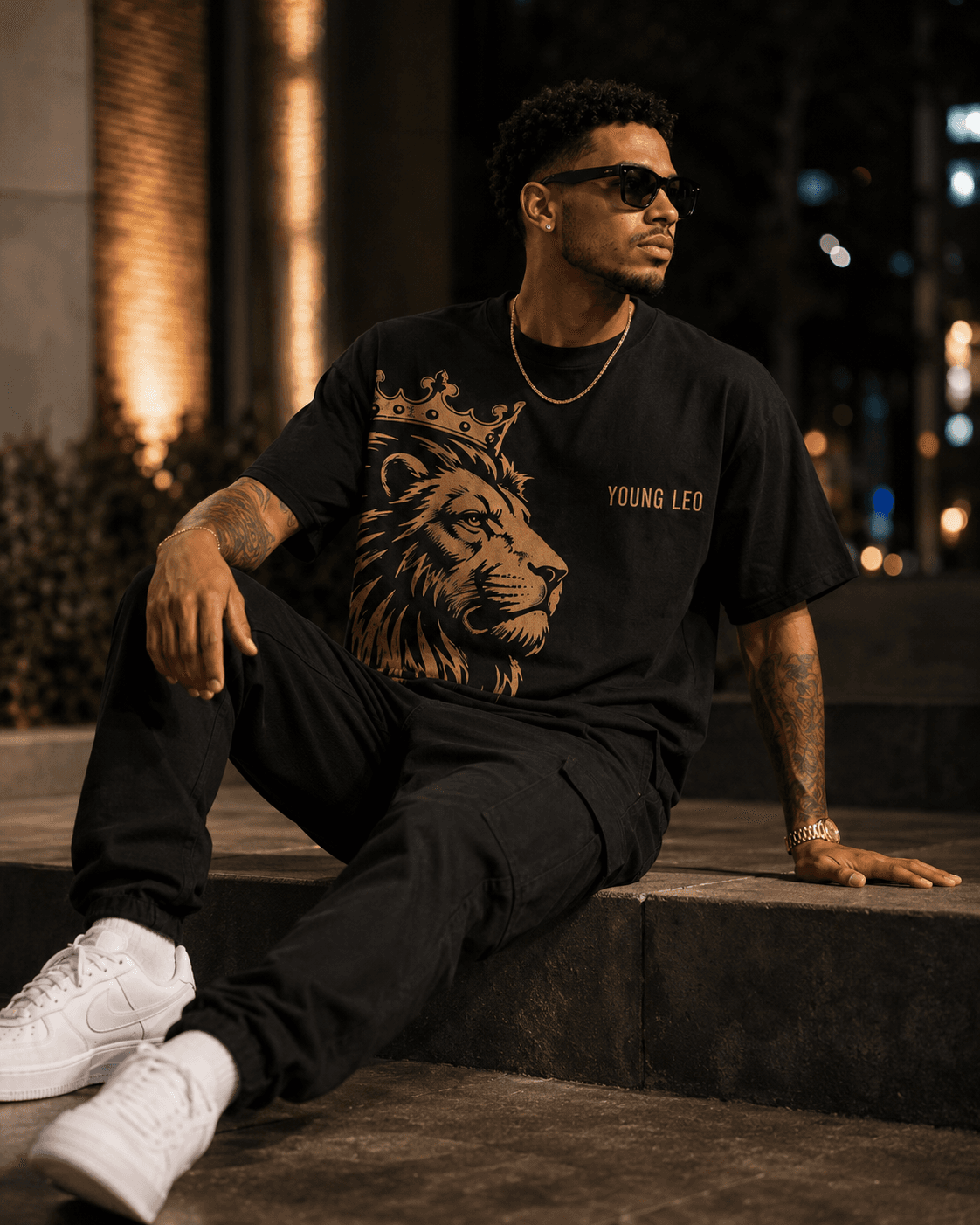 Young Leo — model seated wearing The Becoming Tee, crowned lion front graphic